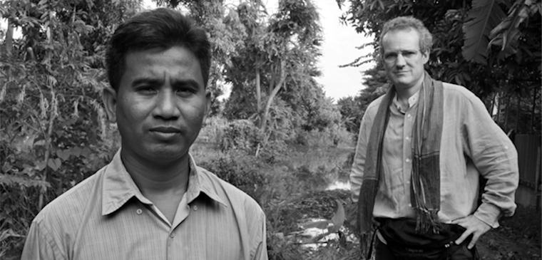 Black and white photograph of two men standing on a path among trees.
