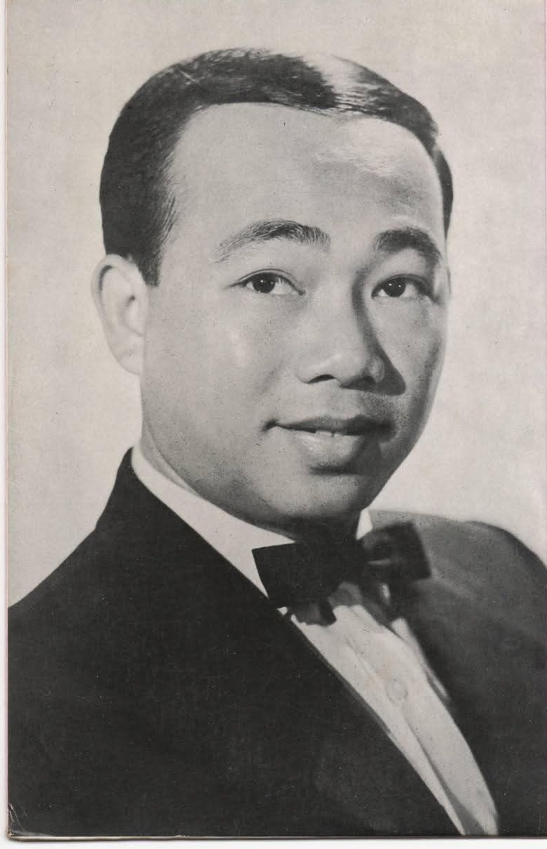 A black-and-white studio portrait of a young man with short dark hair, in a dark jacket, white shirt and bow tie, smiling slightly.