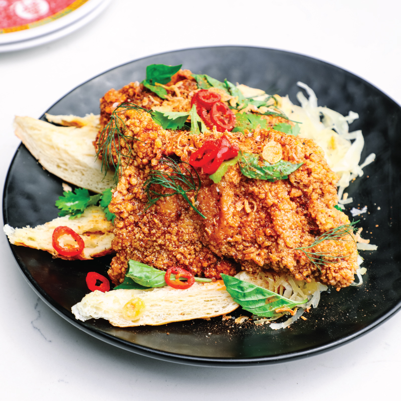 Crispy fried chicken topped with herbs and chili on a black plate.