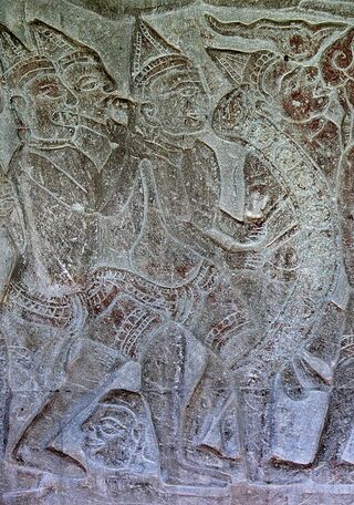 A gray sandstone relief of figures in procession, one carrying a curved frame of gongs.