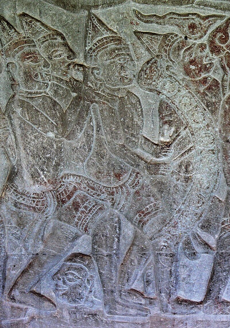 A gray sandstone relief of crowned figures walking in procession, one carrying a long curved frame over his shoulder.