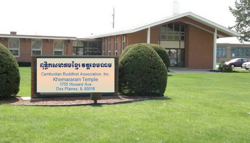 A low brick building behind a lawn and round shrubs, with a sign in Khmer and English in front.