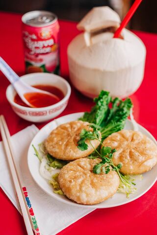 Steamed buns on a plate with herbs and dipping sauce beside a fresh coconut on a red table.