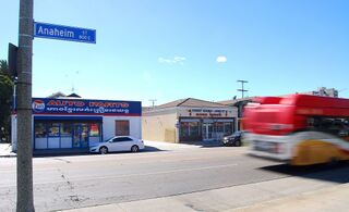 A street corner with an Anaheim Street sign, shops with Khmer and English signs, and a passing bus.