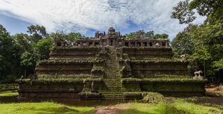 A stepped laterite pyramid temple with a steep central stairway in a grassy clearing.