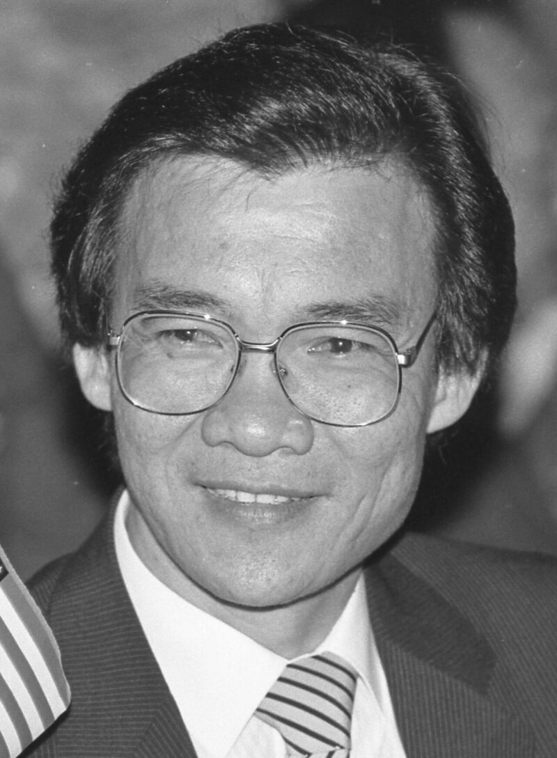 Black-and-white portrait of a smiling man with glasses, in a suit and striped tie.
