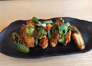 Fried chicken wings topped with sliced chili peppers and green onion on a black plate.