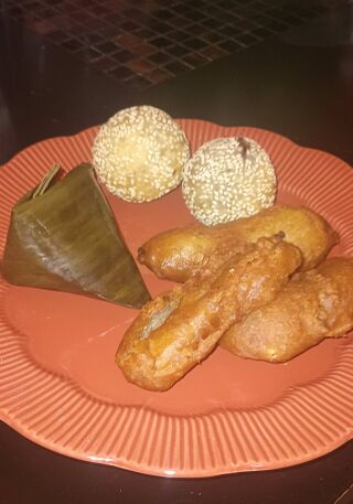 An orange plate with a banana-leaf pyramid, two sesame balls and pieces of fried banana.