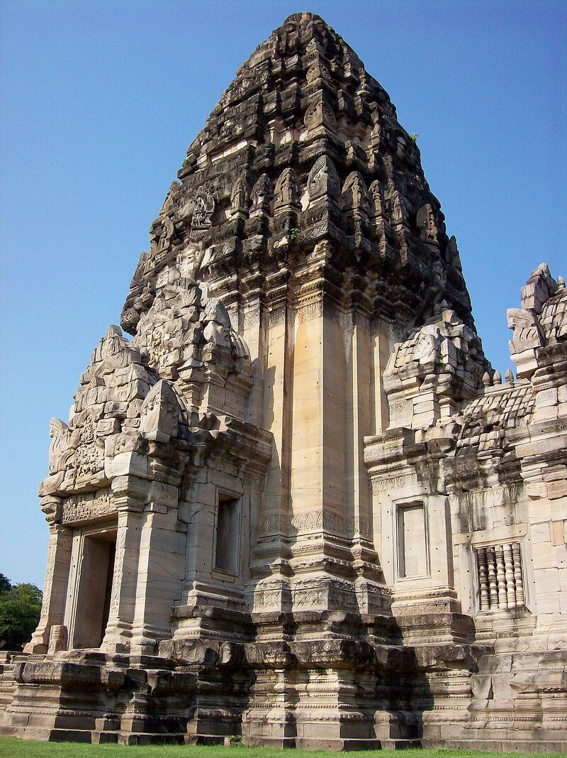 A tall sandstone temple tower with a rounded, carved top and a doorway at its base, under a clear blue sky.