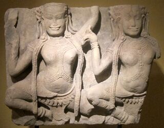 A sandstone relief of two crowned female figures dancing, each with one leg raised.
