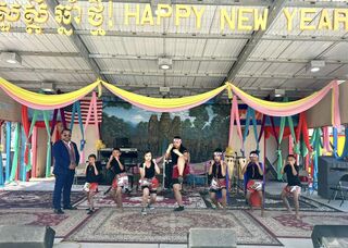 Dancers perform on a stage under a Happy New Year banner hung with colorful drapes.