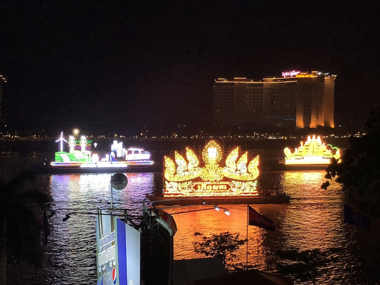 Brightly lit floats glowing on dark water in front of a lit building.