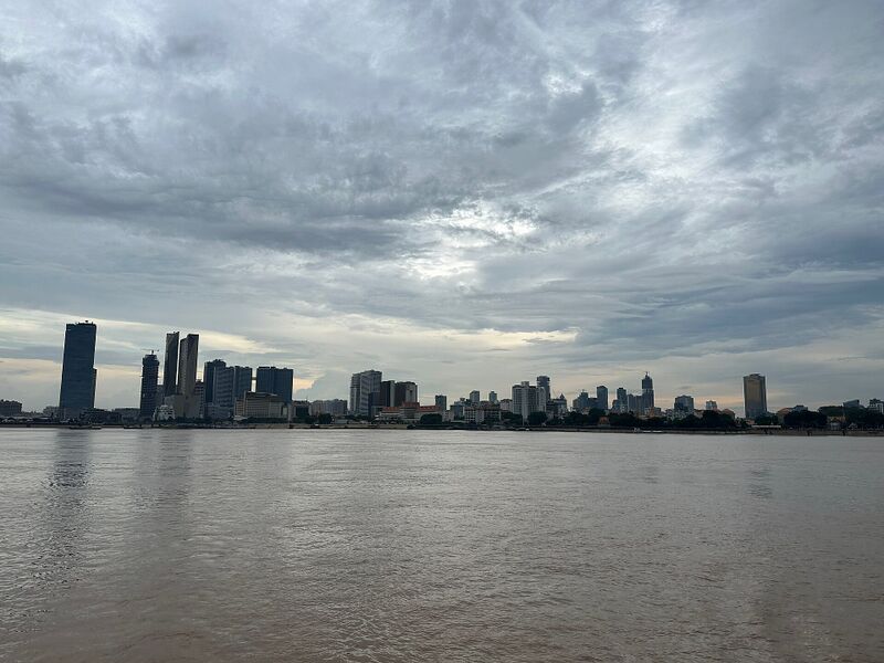 A wide brown river in the foreground, with the towers of a city skyline along the far bank under a heavy gray sky.