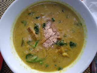 A white bowl of thick yellow-green soup with greens and vegetables.