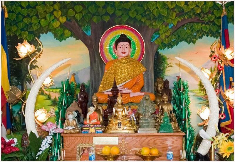 A seated Buddha with a halo before a painted Bodhi tree, smaller Buddhas and offerings on the altar below.