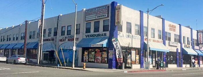 A two-storey corner building with blue awnings over a row of small shops.