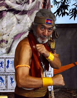 An older man in a krama and headband holding a fighting stance.