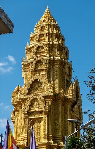 A tall golden stupa carved in tiers, rising against a deep blue sky.