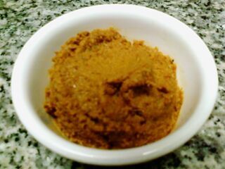 A white bowl filled with a thick reddish-orange spice paste on a granite counter.