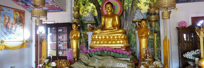 Large gold seated Buddha with two standing disciples, a reclining Buddha in front, lotus decorations and bookcases of scriptures.