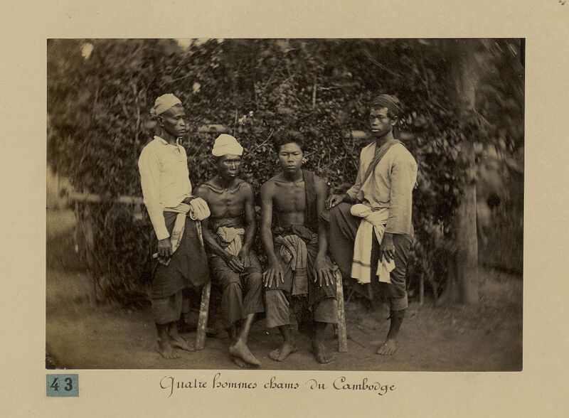 A sepia photograph of four men in sarongs and shirts standing and sitting together.