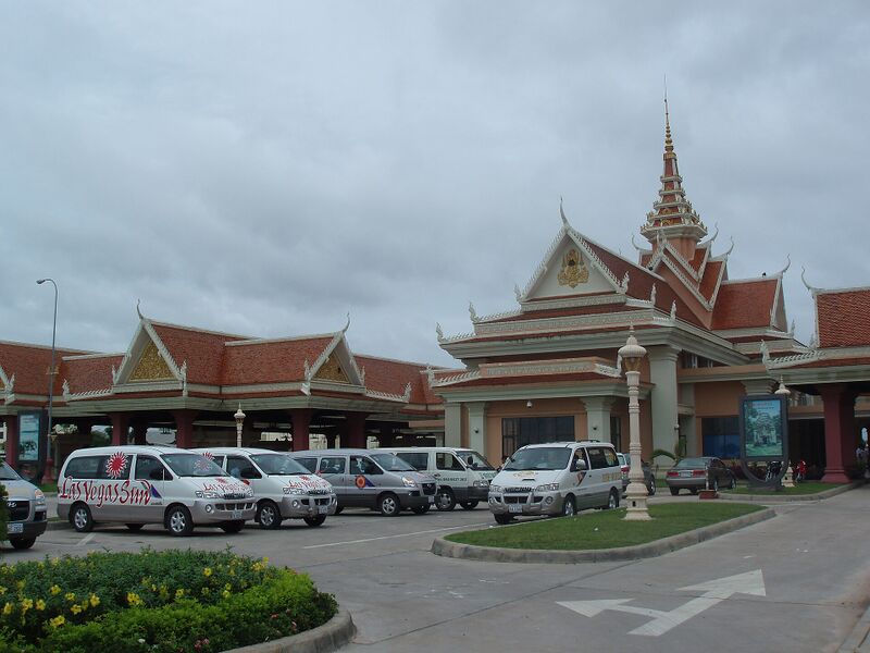 A building with tiered Khmer-style roofs and a spire, with vans parked in front.