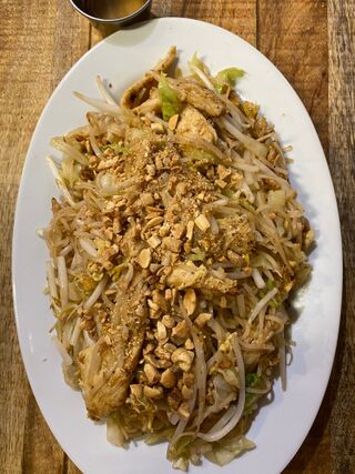Oval white plate of thin stir-fried noodles with bean sprouts and crushed peanuts on a wooden table.