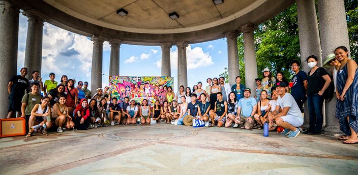 A large group posing in a circle under an open domed pavilion.