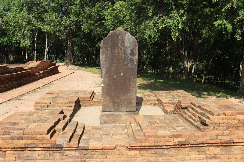 An upright inscribed stone slab standing on a brick platform among trees.