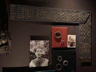A museum case with bangles, armlets and earrings beside a photograph of a dancer in a crown.