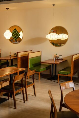 Wooden tables and chairs with green cushioned benches under round hanging lamps and a framed wall emblem.