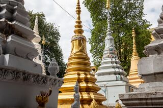 A row of tall white, gold and gray stupas with pointed spires among trees.