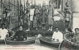 Dancers in crowns and costume standing behind musicians who sit at circular gong frames and xylophones.
