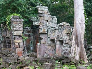 Leaning stone towers and fallen blocks among tall trees in a forest clearing.