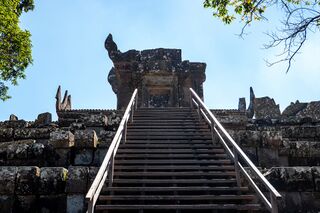 A steep stone stairway with metal handrails rising to a ruined gate pavilion.