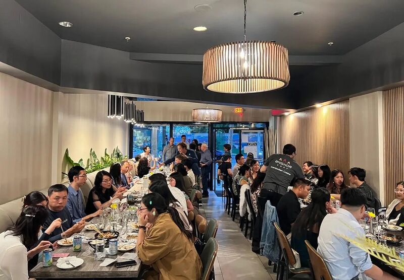 A full restaurant dining room with long tables of diners under a drum pendant lamp.