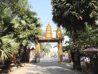 A gateway topped by three golden spires over a street, framed by sugar palms.
