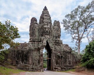 A tall stone gate tower with carved faces above a narrow archway, framed by trees.