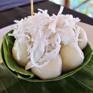 White sticky rice balls under a heap of shredded coconut in a folded banana-leaf cup.
