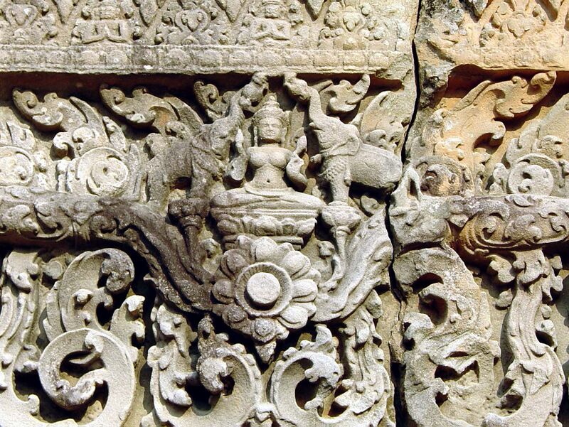 A carved gray sandstone lintel with a small seated goddess at the center, flanked by two elephants raising their trunks over her, above a large lotus medallion and curling foliage.