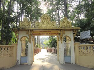 A cream and gold gateway with a carved crest opening onto a straight path through tall trees.