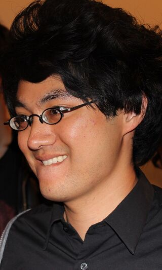 A smiling man with black hair and glasses in a dark shirt, seen in profile.