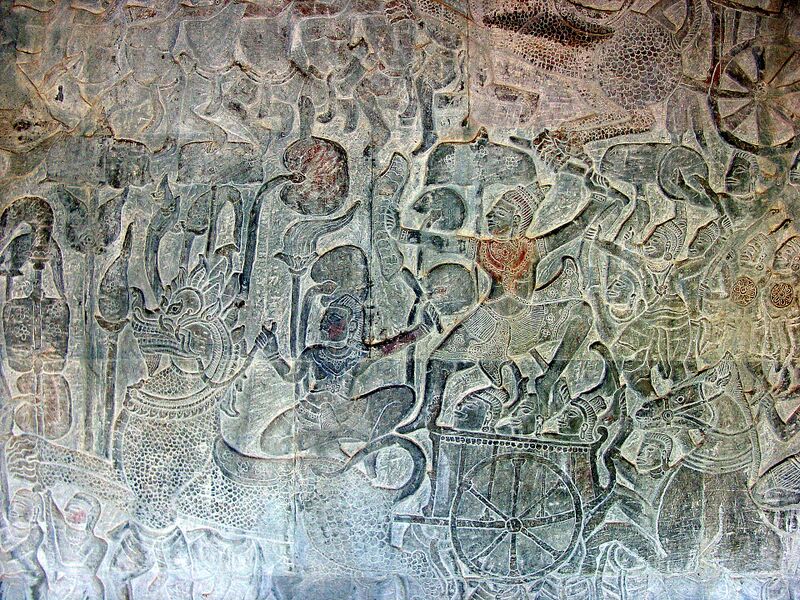A carved stone wall showing a battle scene with a central figure on a mount surrounded by warriors.