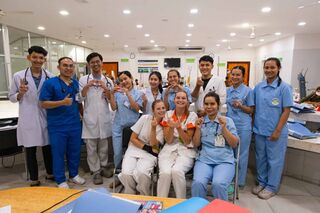 Nurses and doctors in blue and white uniforms stand smiling in a bright room around a table with training materials.