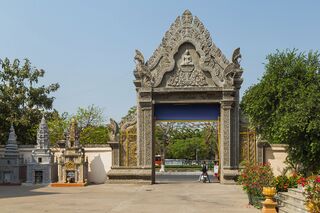 A gray carved stone gateway with a pointed pediment opening onto a paved courtyard.