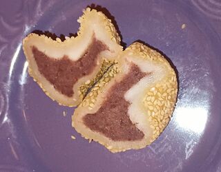 A cut sesame ball revealing a thin crisp shell and a reddish-brown bean filling, on a purple plate.
