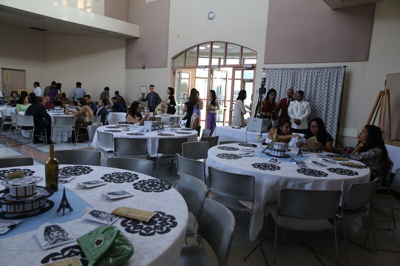 Round banquet tables with black lace-pattern place mats and Eiffel Tower centerpieces in a hall, guests seated and talking near the doors.