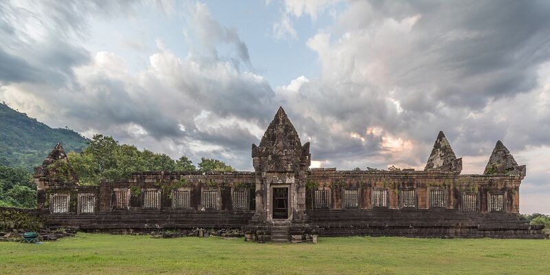 A ruined sandstone palace with gabled towers on a lawn under a cloudy sky.