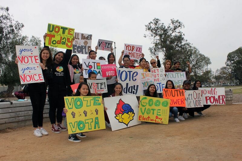 A group of young people holding hand-painted signs urging people to vote.