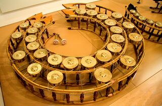 A circular wooden frame holding a ring of small bronze gongs, seen from above.